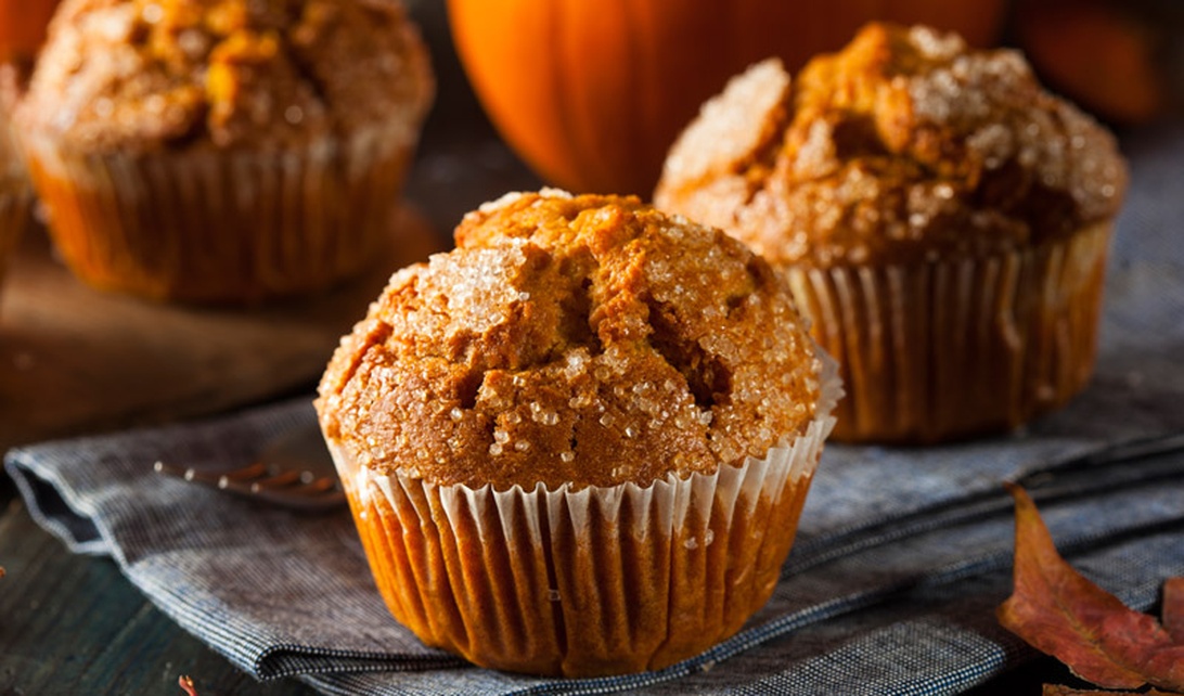 Nybakade pumpamuffins i pappersformar på mörkt underlag med höstdekorationer som pumpa och löv.