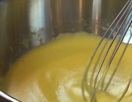 Visp rör en gul sås i en rostfri kastrull på spisen